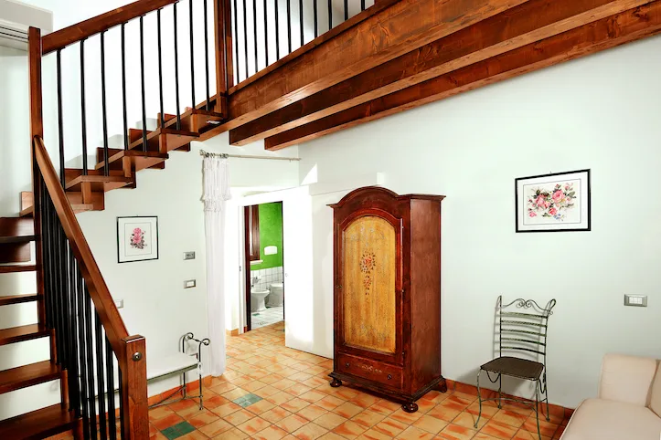 Interno di camera con scala in legno, soppalco e armadio antico dipinto