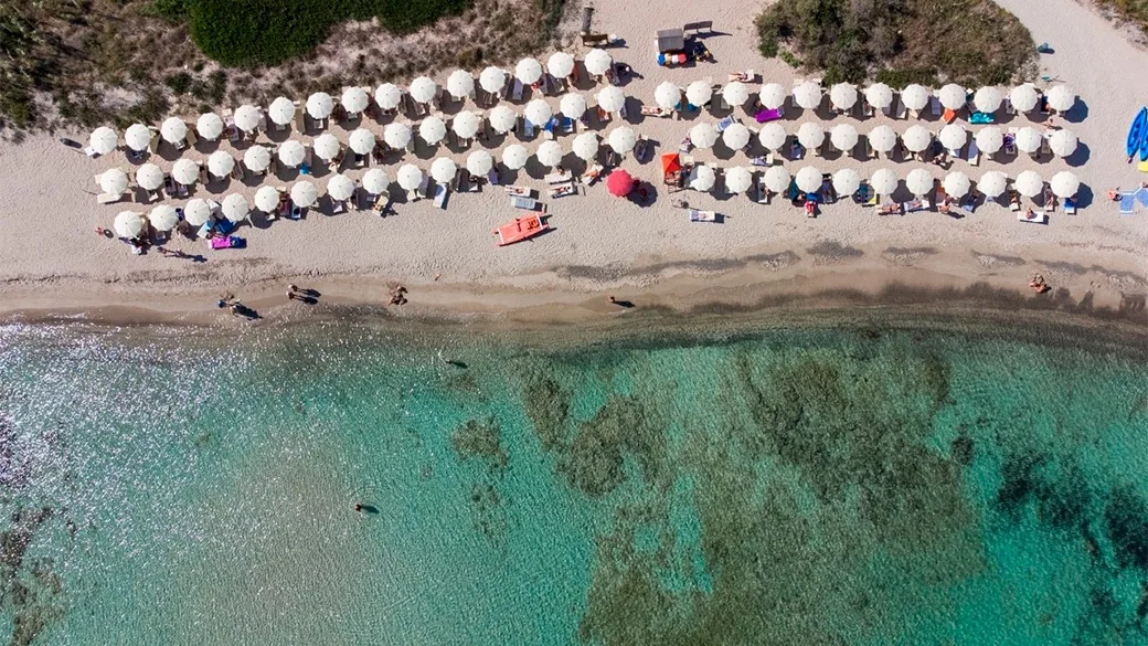 Vista dall'alto delle file di ombrelloni bianchi sulla spiaggia con acqua trasparente