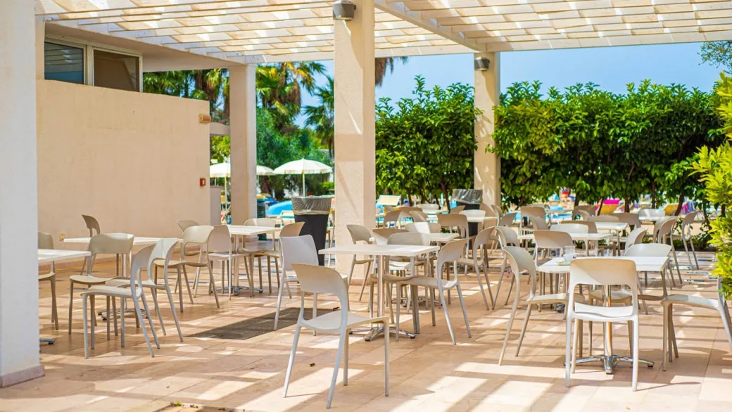Terrazza bar all'aperto con tavoli e sedie bianche sotto pergolato
