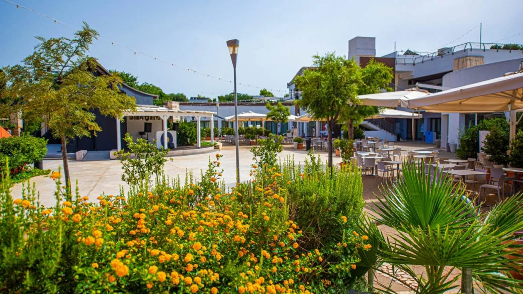 Piazzetta interna del resort con giardino fiorito, tavoli e palco