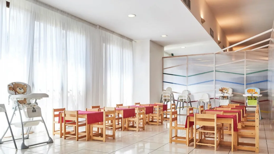 Sala mensa per bambini con tavolini in legno e seggioloni