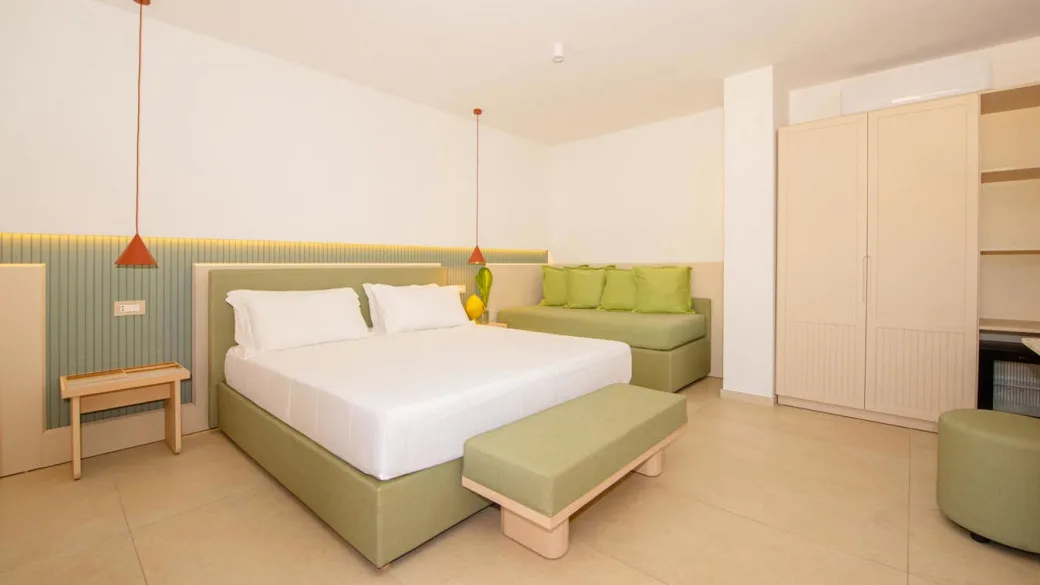 Camera rinnovata con letto matrimoniale, divano verde e arredo moderno