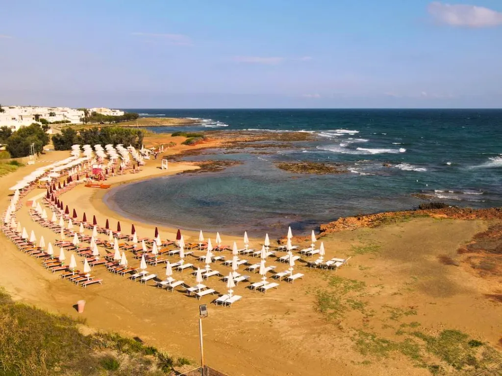 Spiaggia con file di lettini e ombrelloni lungo la costa rocciosa e mare mosso