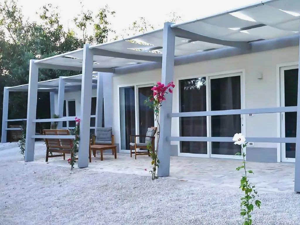 Veranda con pergolato bianco, poltrone in legno e fiori davanti a bungalow moderno