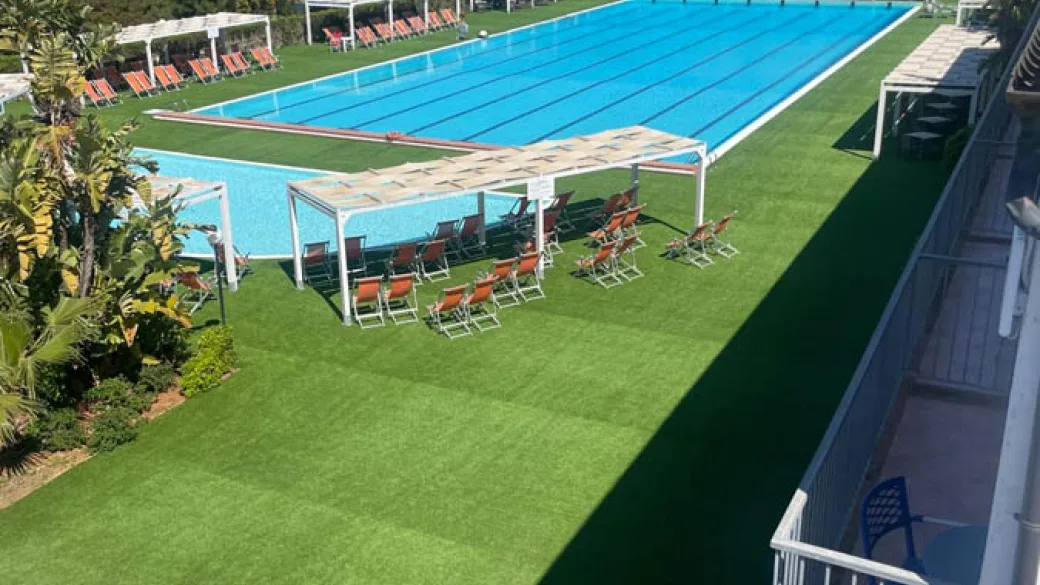 Area relax con lettini arancioni sotto pergolati a bordo piscina su prato verde