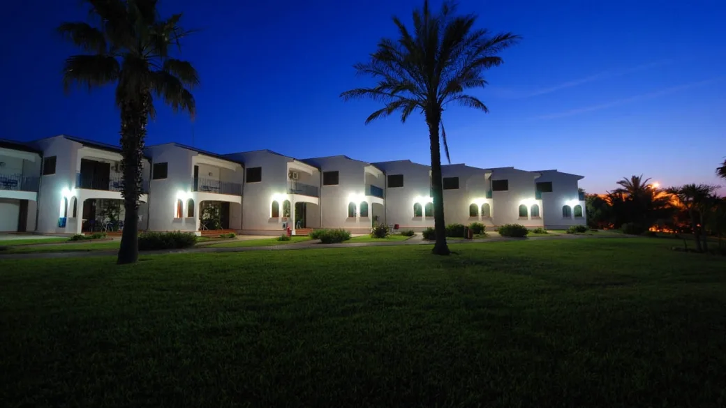 Edificio bianco del resort illuminato di sera con palme in primo piano al crepuscolo