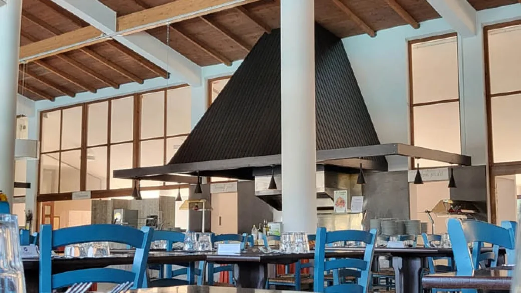 Interno del ristorante con travi in legno, cappe nere e sedie blu apparecchiate