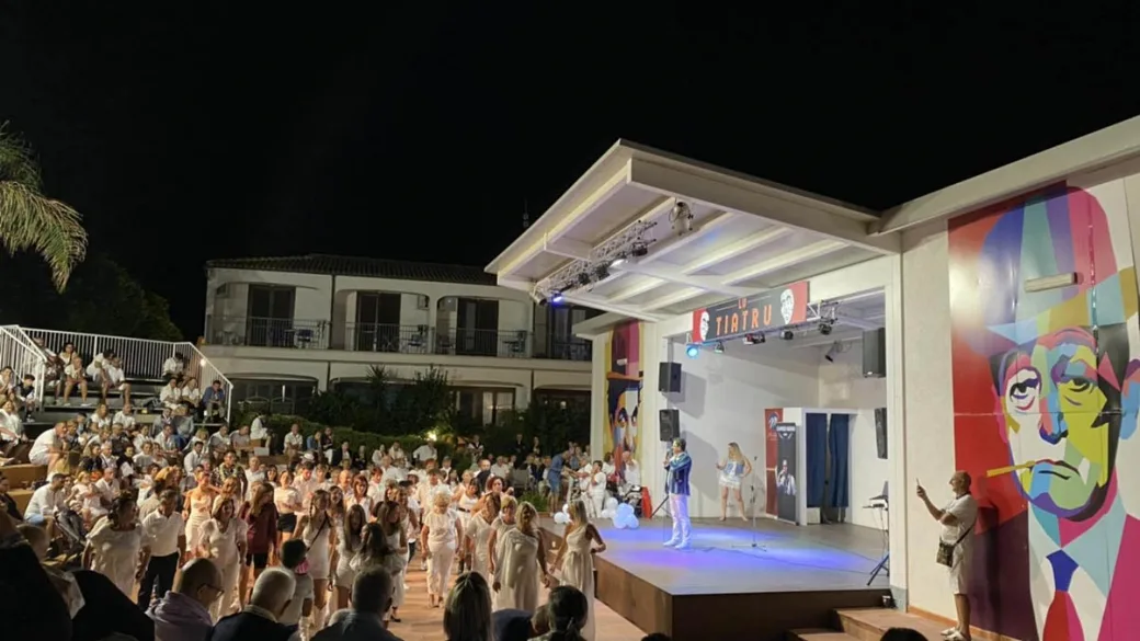 Spettacolo serale all'aperto su palco con pubblico numeroso e murale colorato