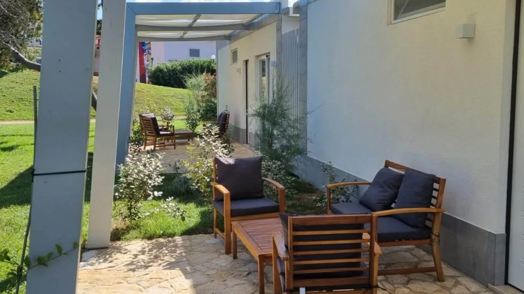 Veranda esterna di bungalow con poltrone in legno, cuscini grigi e pergolato
