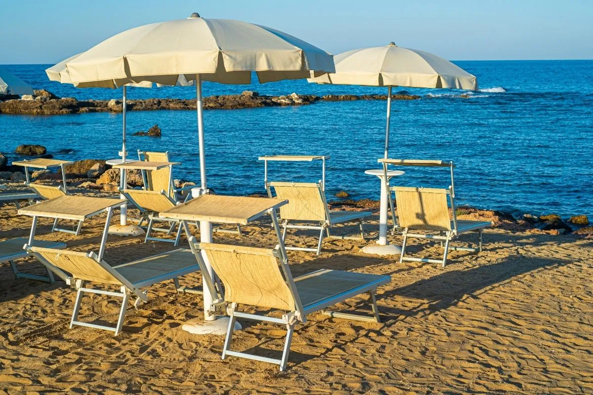 Lettini con ombrelloni bianchi su spiaggia sabbiosa vista mare