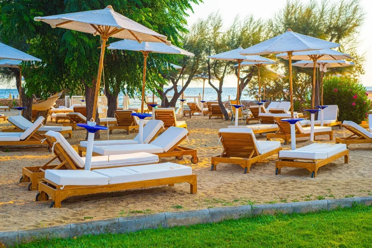 Lettini in legno con ombrelloni bianchi tra gli alberi vicino al mare