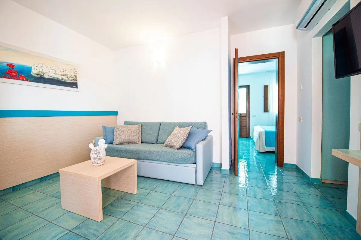 Soggiorno di camera con divano azzurro e camera da letto attigua