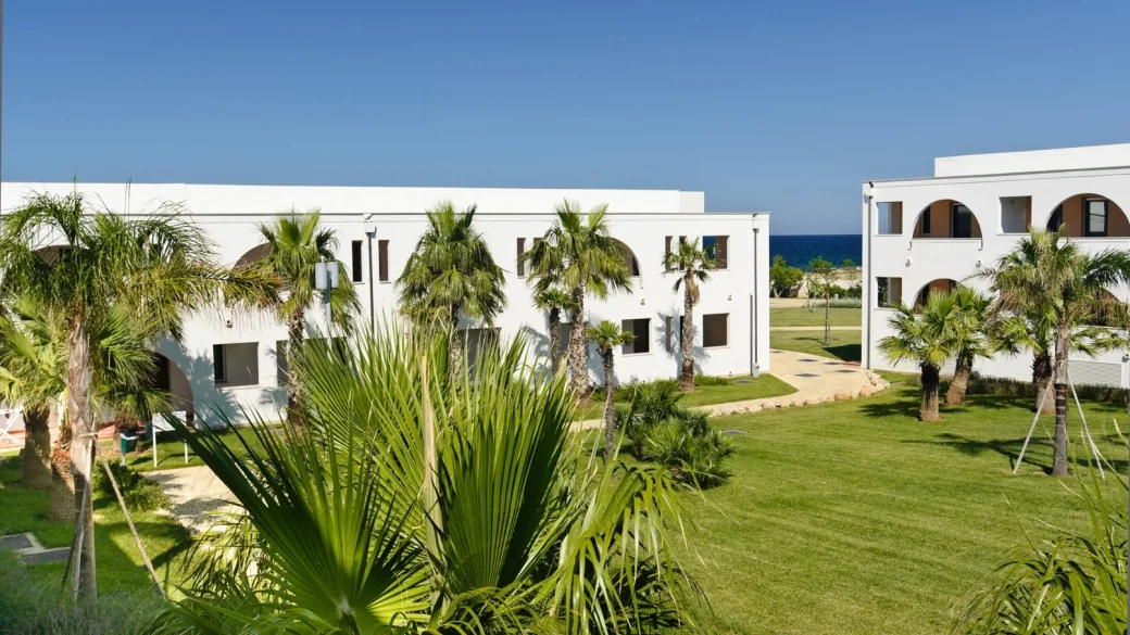 Edifici bianchi ad archi con palme e giardino affacciati sul mare