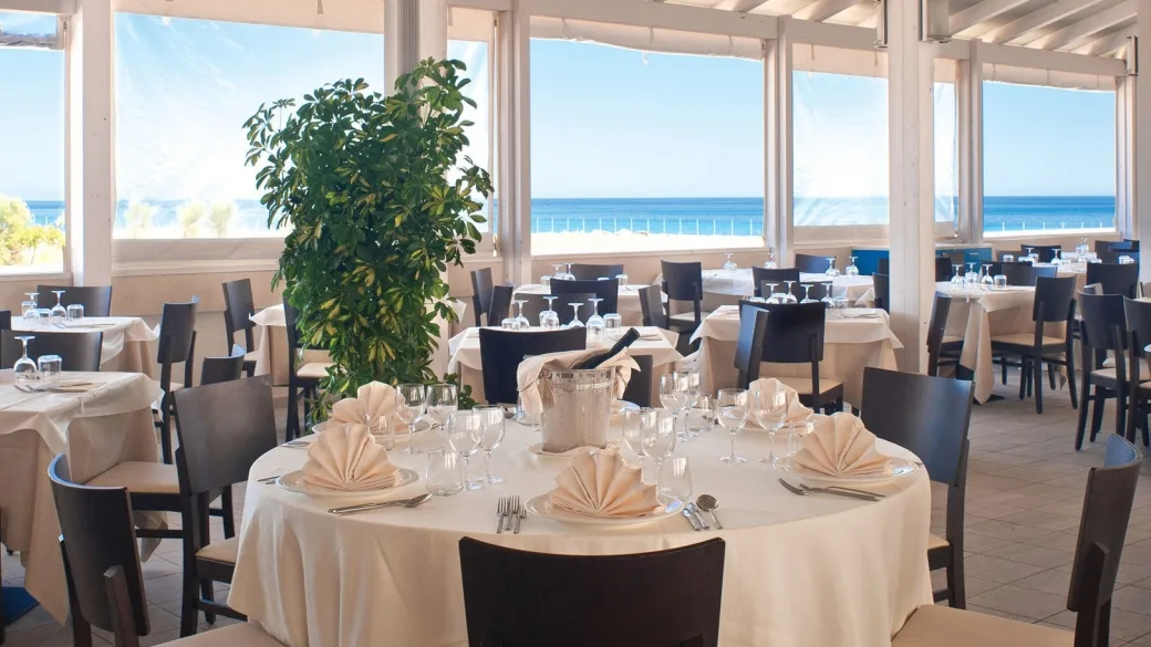 Sala ristorante con tavoli apparecchiati e ampie vetrate vista mare