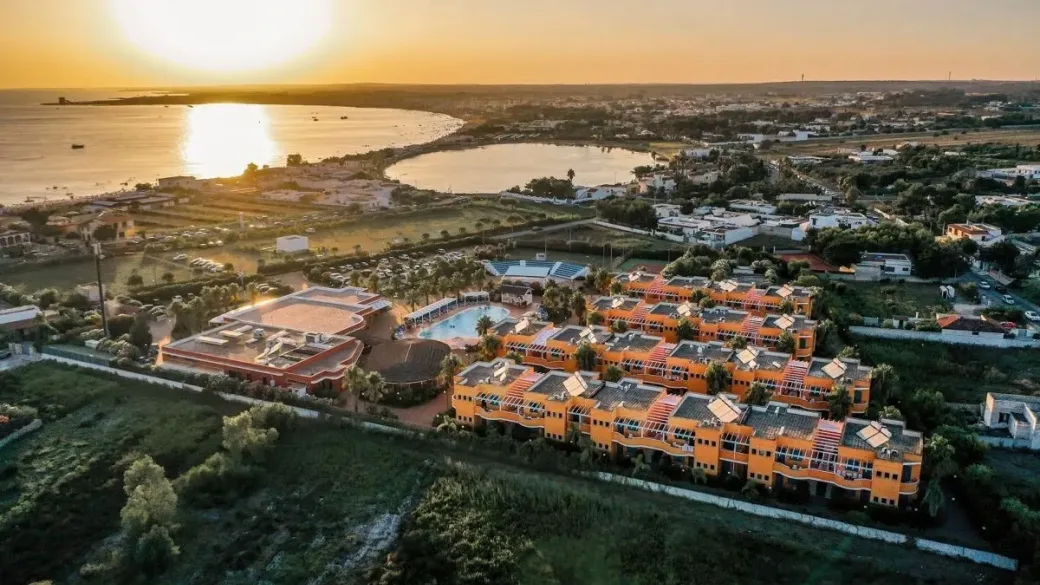 Vista aerea del resort con edifici arancioni e piscina al tramonto vicino alla baia