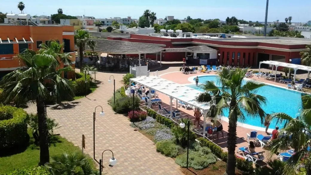 Area piscina del resort con lettini, palme e giardino curato