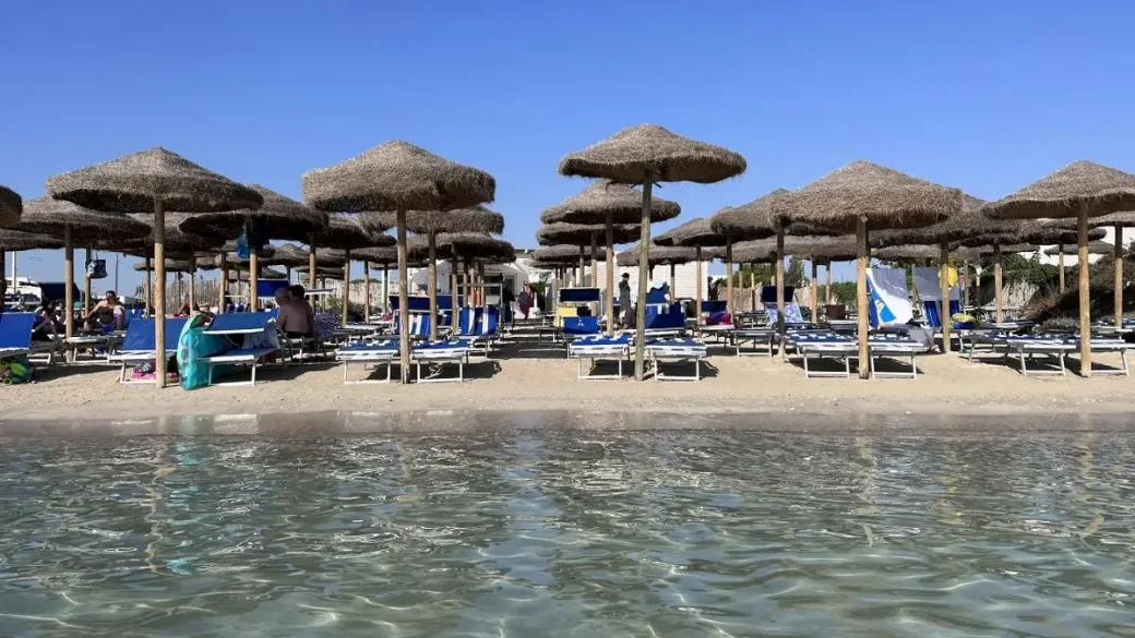 Spiaggia con ombrelloni in paglia e lettini blu vista dal mare