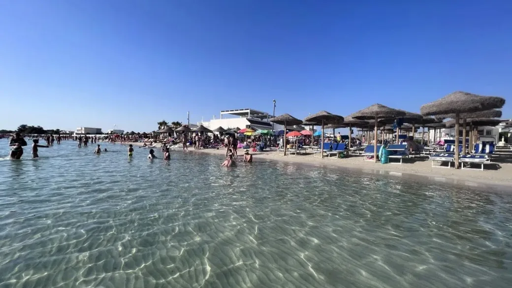 Spiaggia affollata con bagnanti e acqua trasparente
