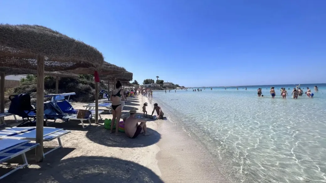 Bagnanti sulla spiaggia con ombrelloni in paglia e mare turchese