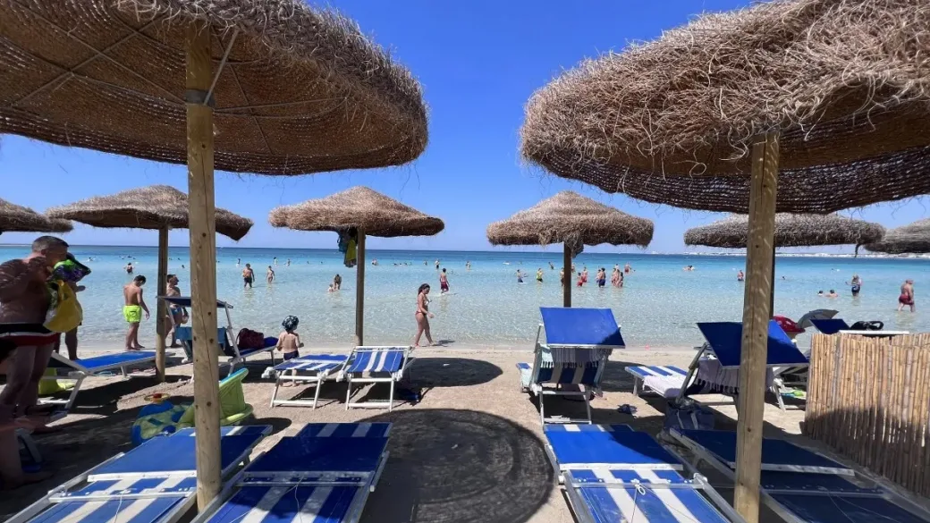 Ombrelloni in paglia e lettini blu sulla spiaggia con mare limpido