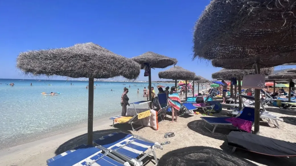 Spiaggia con ombrelloni in paglia e turisti in acqua turchese