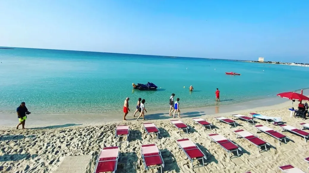 Spiaggia con lettini rossi, moto d'acqua e mare azzurro