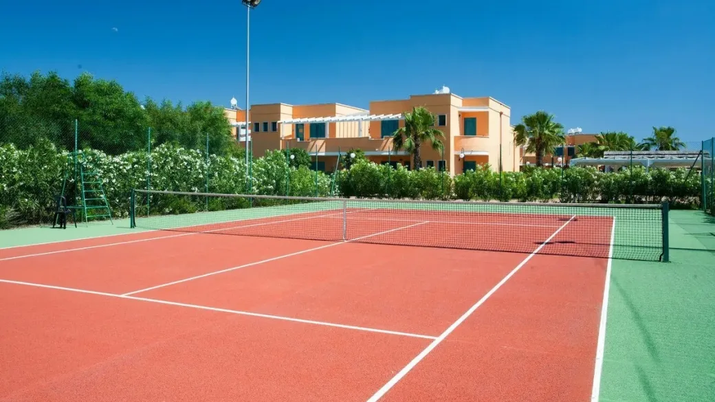 Campo da tennis in terra rossa con edifici del resort sullo sfondo