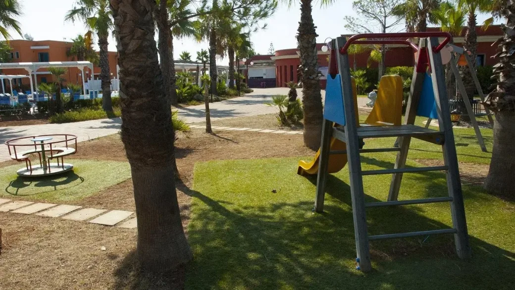 Parco giochi per bambini con scivolo e giostrina tra le palme