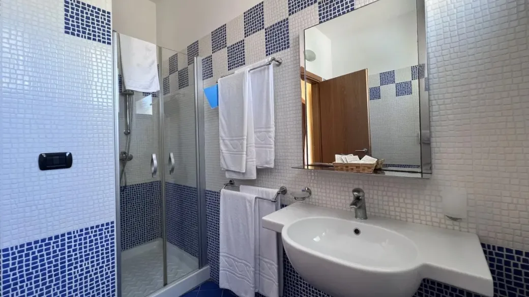 Bagno con doccia, lavabo e piastrelle a mosaico blu e bianco