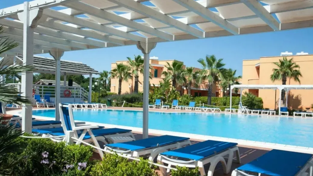 Piscina con pergolato bianco e lettini blu tra le palme