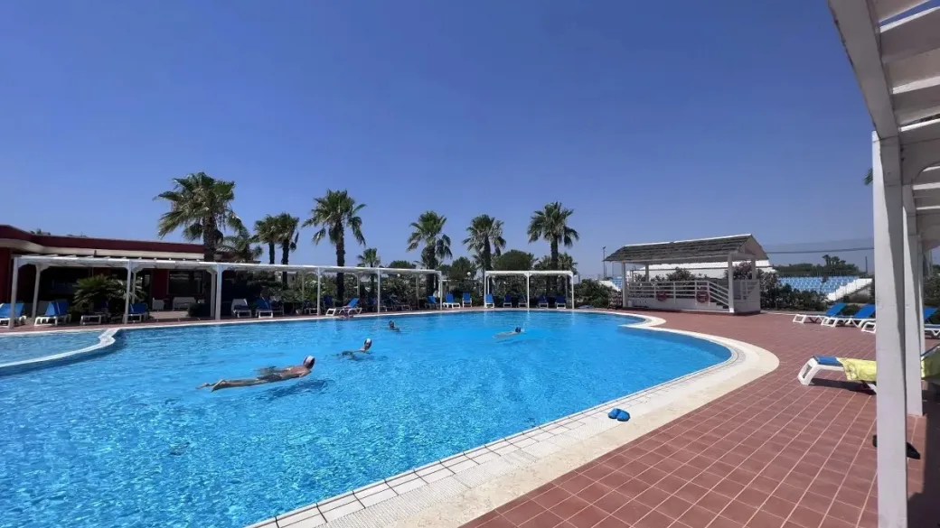 Piscina con nuotatori, lettini blu e palme