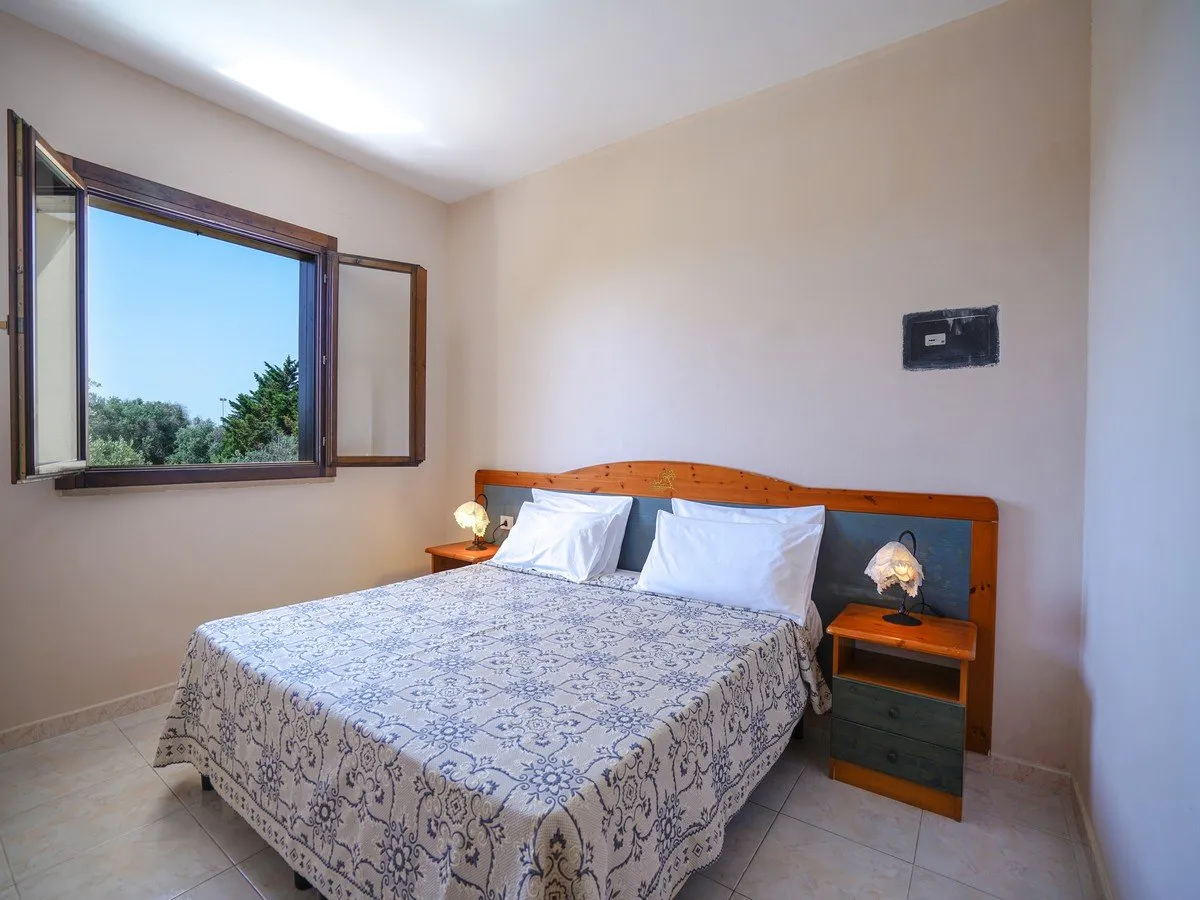 Camera da letto matrimoniale con copriletto decorato, comodini in legno e finestra con vista sul verde
