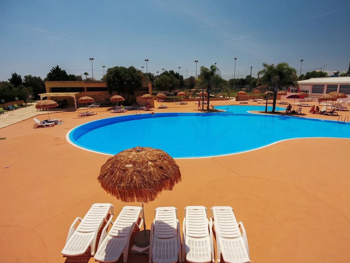 Piscina a forma libera vista dall'alto con lettini bianchi e ombrelloni in paglia
