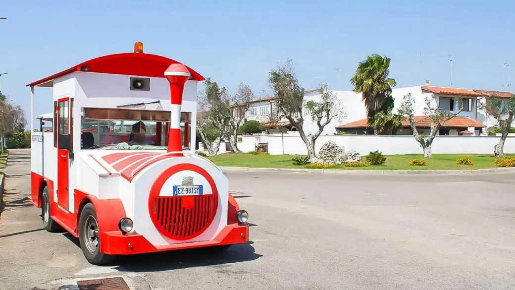 Trenino turistico bianco e rosso lungo la strada del villaggio con abitazioni sullo sfondo