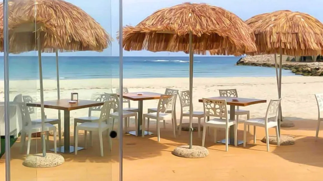 Tavoli con ombrelloni in paglia vista mare e spiaggia sabbiosa