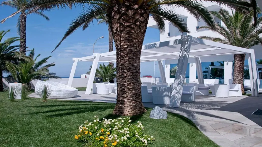Giardino curato con palme, fiori e zona lounge esterna con gazebo bianco vista mare
