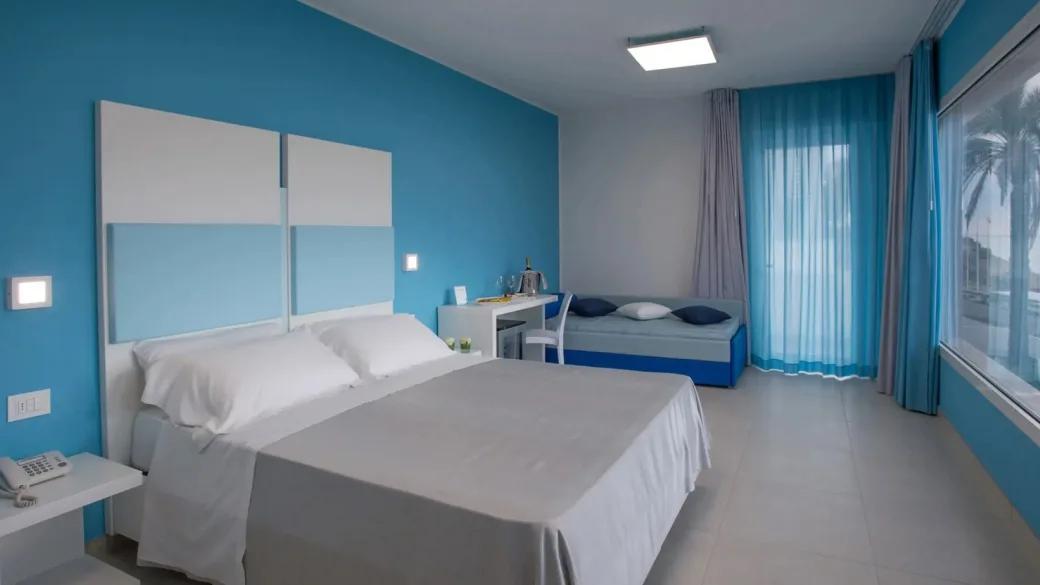 Camera matrimoniale con parete azzurra, letto bianco e divanetto blu