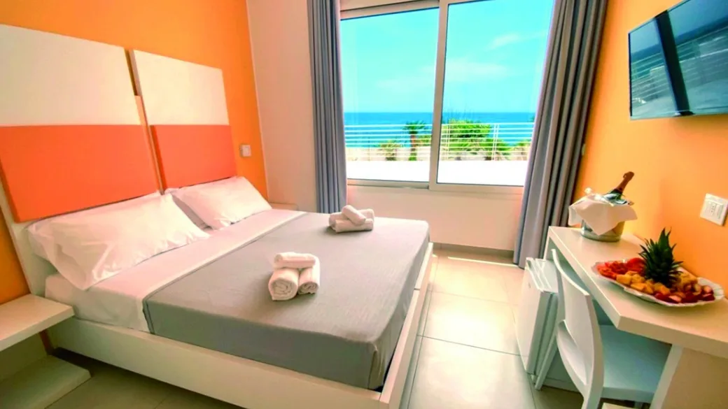 Camera con pareti arancioni, letto matrimoniale e vista mare dalla finestra