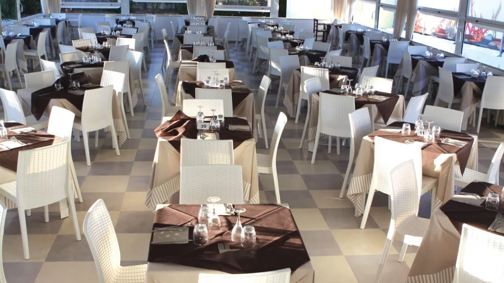 Sala ristorante interna con tavoli apparecchiati, tovaglie marroni e sedie bianche