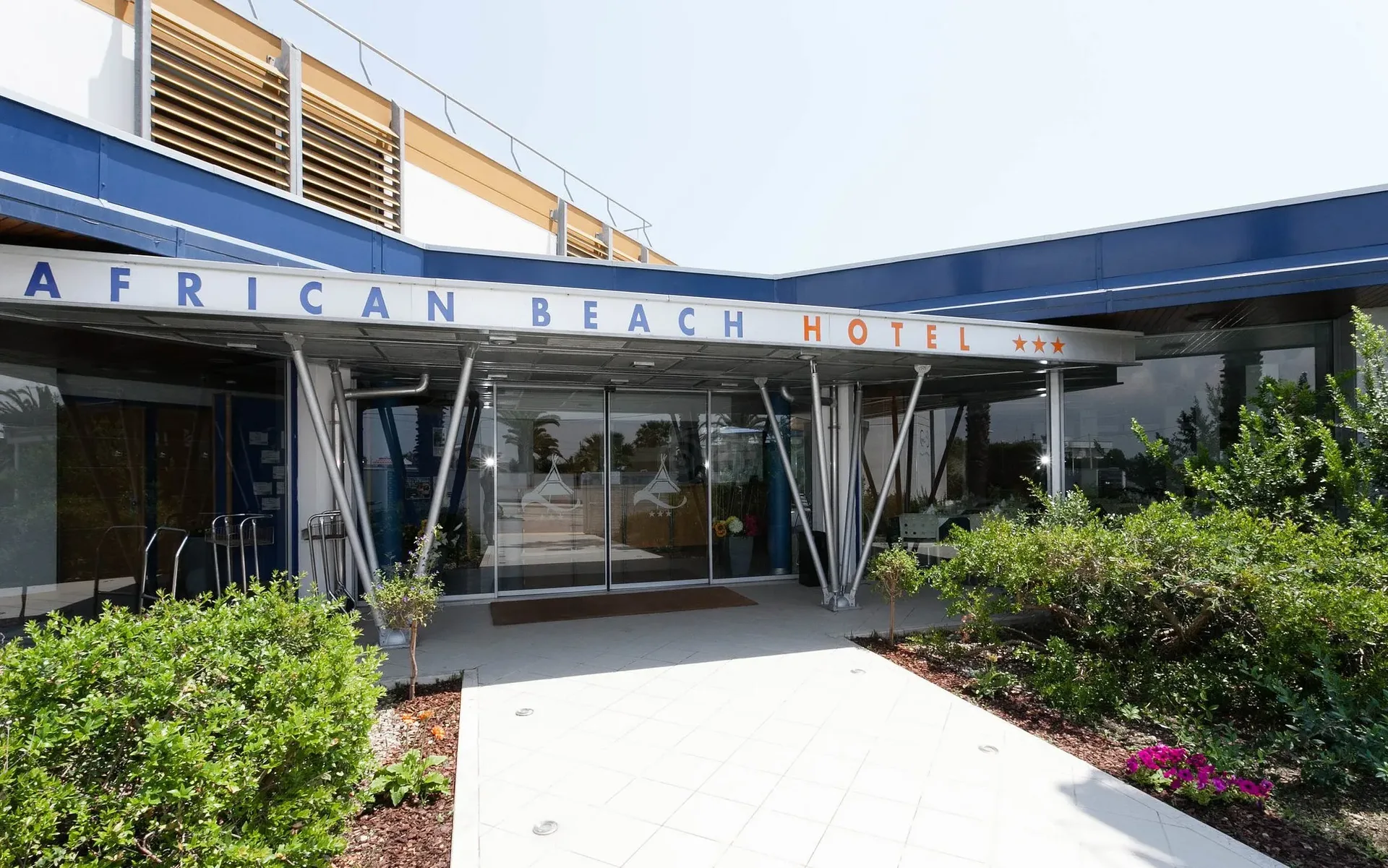 Ingresso dell'African Beach Hotel con insegna e porte scorrevoli in vetro circondate dal verde