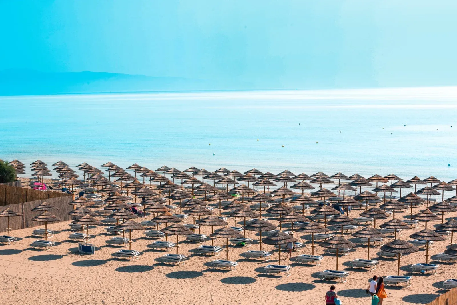 Spiaggia sabbiosa con file di ombrelloni in paglia e mare azzurro