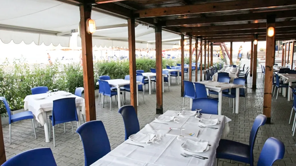 Ristorante all'aperto con pergolato in legno, tovaglie bianche e sedie blu