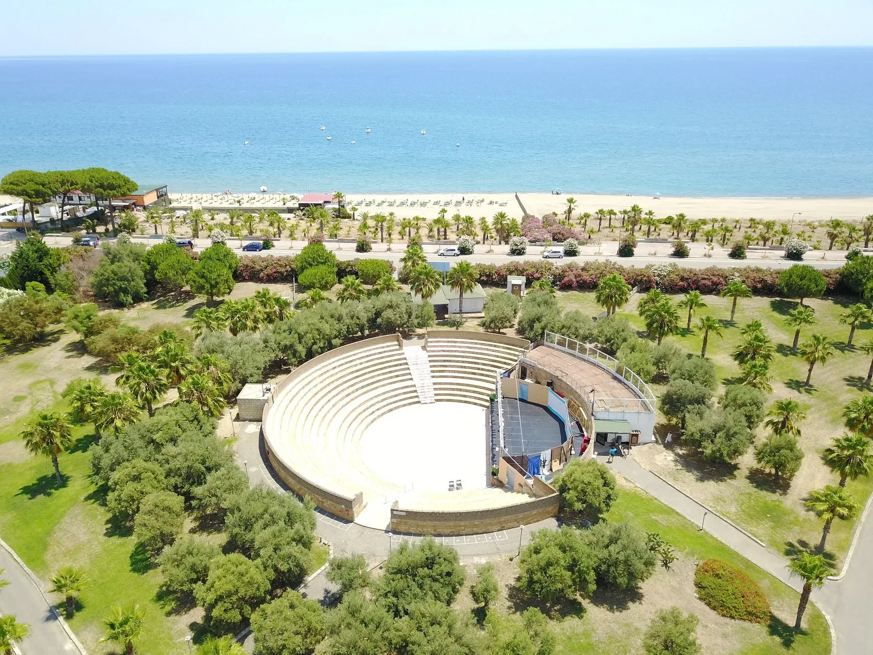 Anfiteatro all'aperto immerso tra palme e ulivi con la spiaggia sullo sfondo
