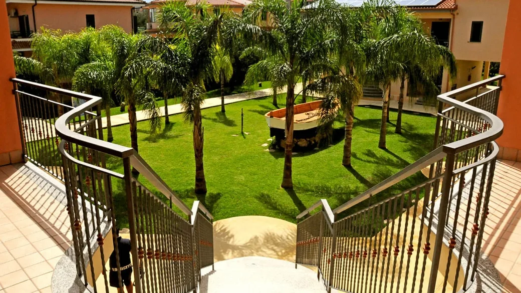 Cortile interno con palme, prato verde e barca decorativa visto dalla scalinata