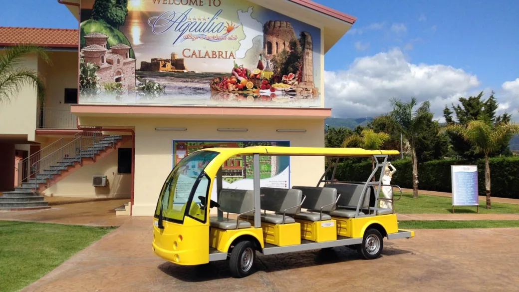 Navetta elettrica gialla davanti all'edificio con insegna del villaggio in Calabria