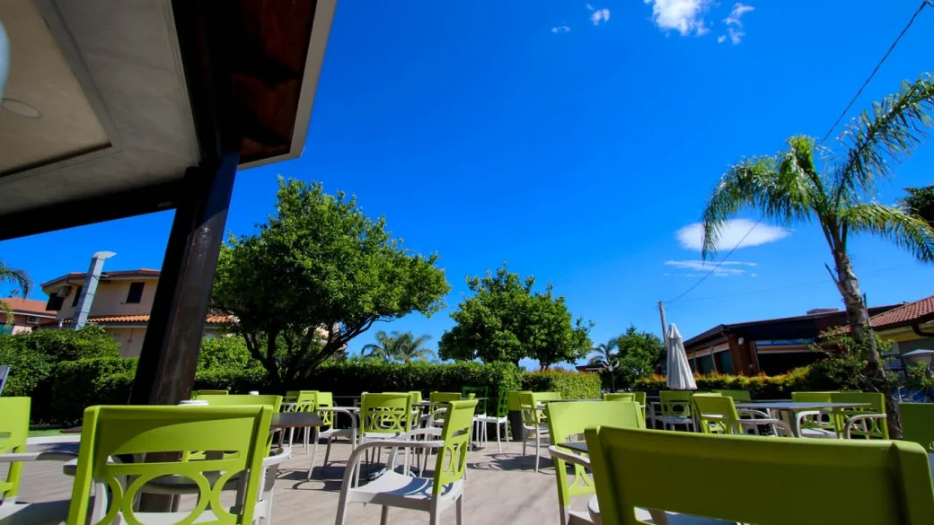 Terrazza esterna del ristorante con sedie verdi e tavoli sotto il cielo azzurro