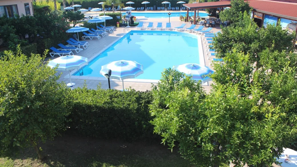 Piscina con lettini blu e ombrelloni vista tra la vegetazione