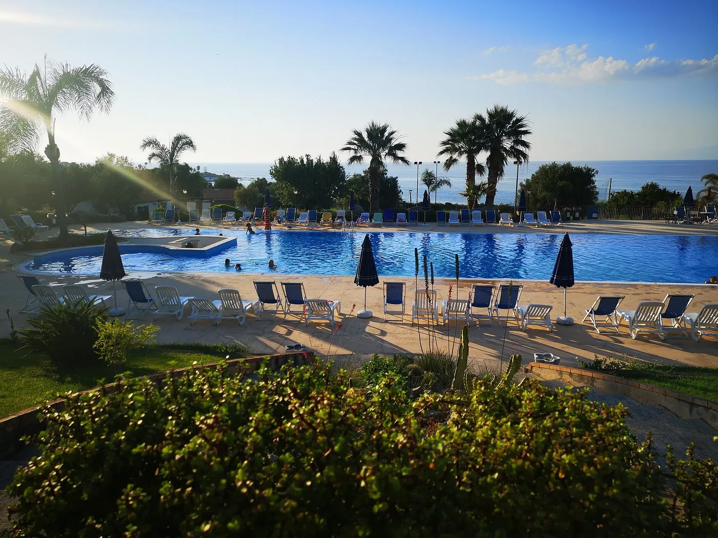 Piscina con lettini e palme al tramonto con vista sul mare