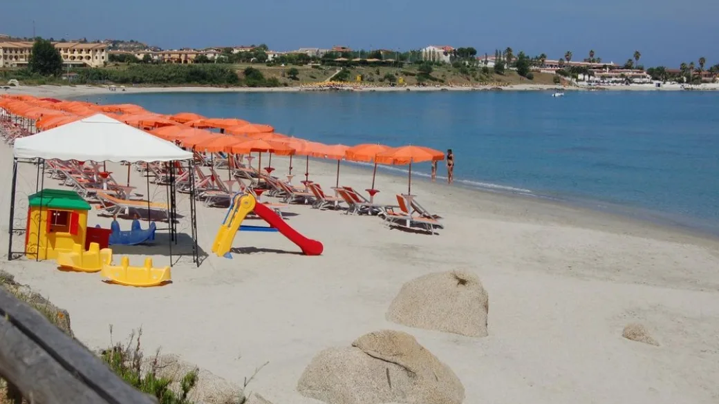 Spiaggia con ombrelloni arancioni e area giochi bimbi sulla riva