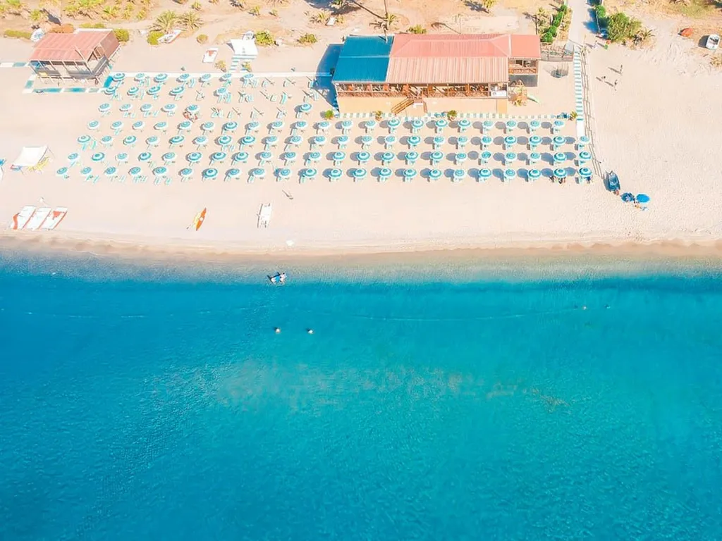 Veduta aerea del lido con ombrelloni, chiosco e mare cristallino